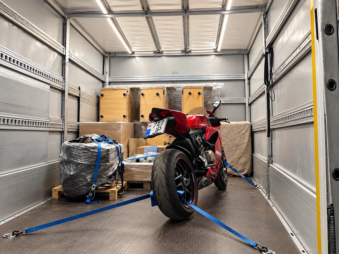 Raudonas „Ducati“ motociklas, pritvirtintas diržais tarp siuntų furgono kėbule