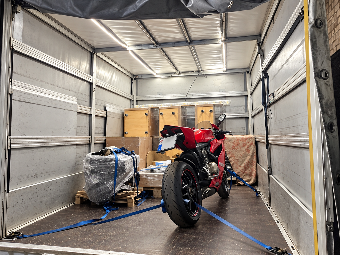 Raudonas „Ducati“ motociklas, pritvirtintas diržais furgono krovinių skyriuje